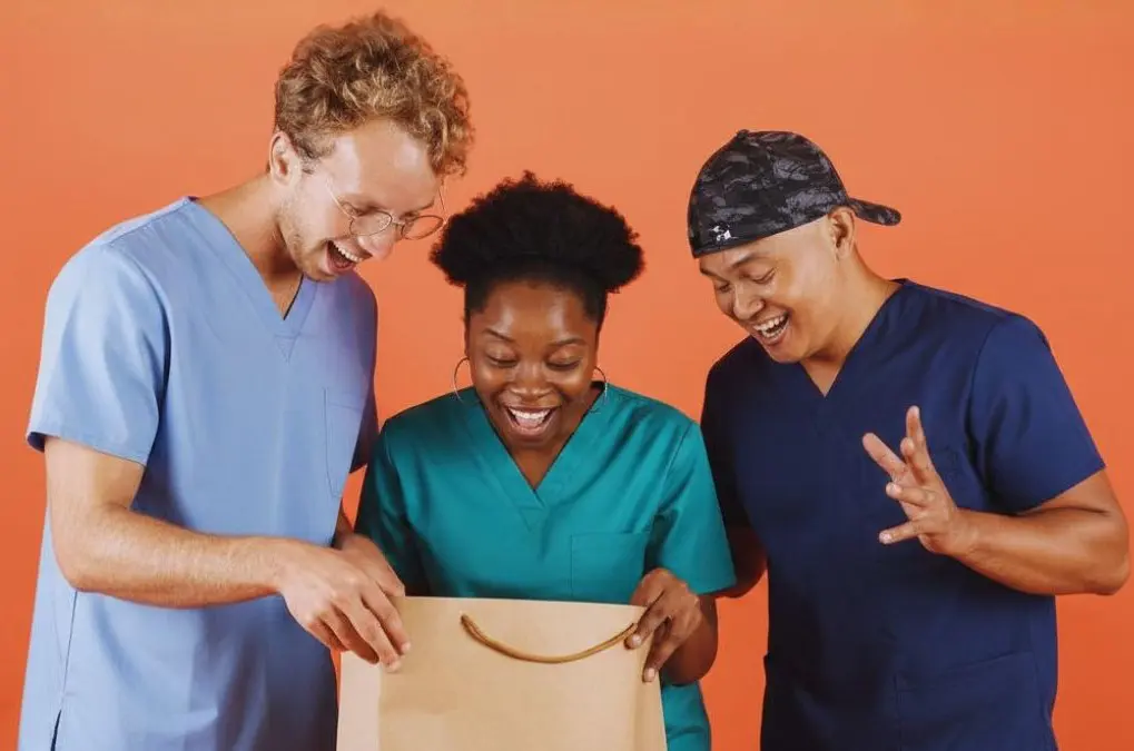 Three people in scrubs looking into a shopping bag together.