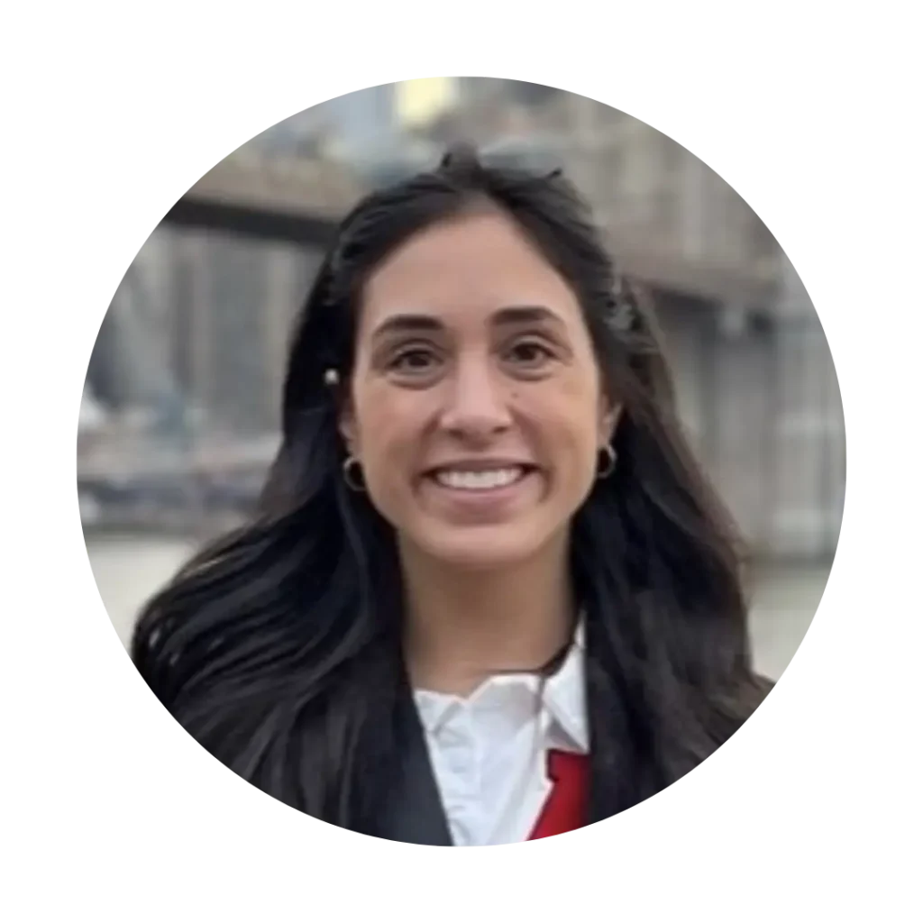 A headshot of Kaitlyn Singh outdoors. Kaitlyn has long dark hair, and wearing a black blazer.